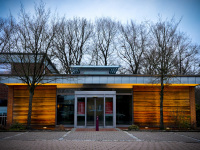 in front of bare oaks stands the nice illuminated wooden building of the sparkasse in unterlüß in lower saxony
