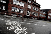 there are painted many white numbers on a schoolyard, in the background you see the red building of the hinrich-wolff-school in bergen in lower saxony