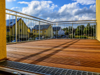 a terrace with wooden planks and metall railings in front of a blue sky with some white clowds