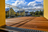 a terrace with wooden planks and metall railings in front of a blue sky with some white clowds