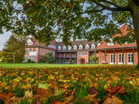 behind a lawn with autumn leaves you see the red building of the evangelical education center in hermannsburg in lower saxony