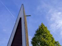 a green tree, a plane and the tower of the catholic church of the resurrection in hermannsburg in lower saxony in front of a blue sky