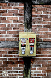 an old yellow gumball machine hangs on a facade of a half-timbered house with red bricks