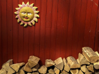 a smiling sun of ceramics and firewood in front of a red wooden wall