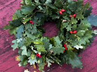 a wreath of oak leaves and rose hips lays on a red wooden table