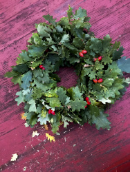 a wreath of oak leaves and rose hips lays on a red wooden table