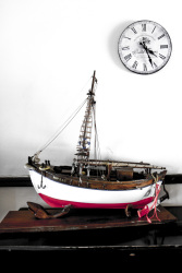 an old clock and a model boat in front of a white wall in the elafos hotel on rhodes