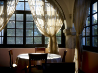 a table with four wooden chairs in front of airy curtains and lattice windows in the elafos hotel on rhodes