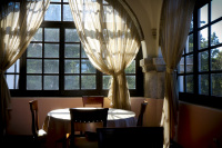 a table with four wooden chairs in front of airy curtains and lattice windows in the elafos hotel on rhodes