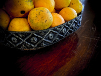 a black metal bowl on a dark brown wooden table is filled with fresh oranges in the elafos hotel on rhodes