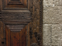 a grey stony wall and a dark brown wooden door with ornaments
