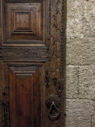 a grey stony wall and a dark brown wooden door with ornaments