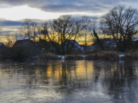 in a sunset light there are some houses behind a frozen lake
