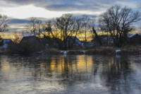 in a sunset light there are some houses behind a frozen lake