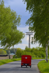 a red piaggio ape 50 is driving on a lonely street along some birch trees straight to a television tower