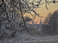 in a white snow landscape at sunset you see the tower of a church in the distance