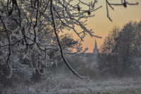 in a white snow landscape at sunset you see the tower of a church in the distance