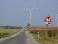 a road between agricultural fields with wind turbines