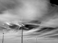 four wind turbines in front of a sky with wild clouds, black-and-white