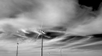 four wind turbines in front of a sky with wild clouds, black-and-white