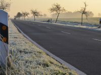 next to a guide post a road runs along through meadows with hoarfrost