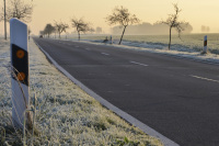 next to a guide post a road runs along through meadows with hoarfrost
