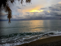 shallow waves on the seashore of the gulf of corinth with a sunset and clouds in the background