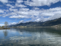 the blue sky, white clouds and green hills are reflecting in the lake pamvotida in ioannina