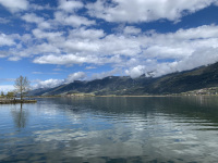 the blue sky, white clouds and green hills are reflecting in the lake pamvotida in ioannina