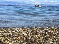 shiny stones at the crystal clear sea of the gulf of corinth where a white fisher boat is swimming