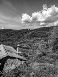 an old house in a hilly landscape and a bright sky with some clouds, black-and-white