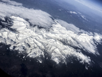 a snow-covered mountain range with some clouds from above