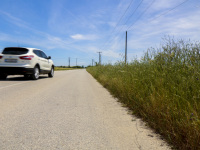 a white suv drives past grain fields on a country road