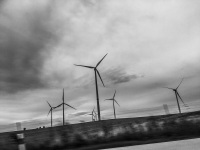 some wind turbines are standing next to a highway by cloudy weather, black-and-white