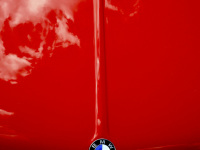 clowds are reflecting in the red shiny engine hood of a bmw e28