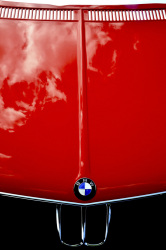 clowds are reflecting in the red shiny engine hood of a bmw e28