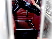 view through an oldtimers quarter window to a black steering wheel and red leather garniture inside
