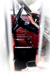 view through an oldtimers quarter window to a black steering wheel and red leather garniture inside