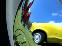 a yellow ford oldtimer is reflecting in a chrome rim of a whitewall tire of a vw