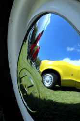 a yellow ford oldtimer is reflecting in a chrome rim of a whitewall tire of a vw