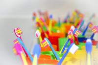 a lot of colorful children\'s toothbrushes are standing in also colorful toothbrush cups