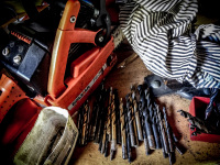 an orange dolmar chainsaw, various drills and a peace of an old shirt are laying in a workshop