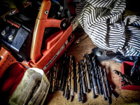 an orange dolmar chainsaw, various drills and a peace of an old shirt are laying in a workshop