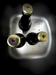 three bottles of astra pilsener are standing in a stainless steel sink
