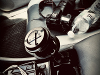 a camera, a lens, a bottle water and a cup of coffee on the passenger seat in a mercedes clk