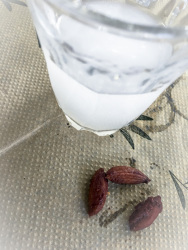 a glass of ouzo and three olivestones on a papier tablecloth with olive design