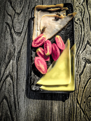 a plate with cheese, ham, tomatoes and two wasps is standing on a wooden table