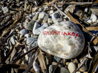 on a stony beach is laying a stone with red lettering olympiakos