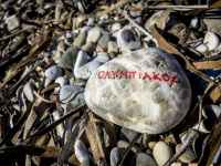 on a stony beach is laying a stone with red lettering olympiakos