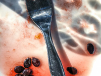 a silver fork is laying on a white plate with red juice and seeds of a watermelon